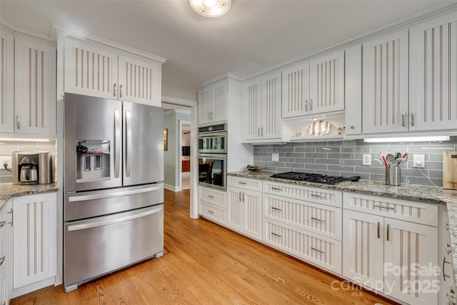 kitchen featuring light wood-style floors, appliances with stainless steel finishes, backsplash, and light stone countertops