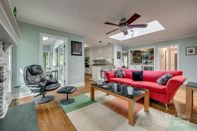 living room featuring light wood-type flooring, ornamental molding, a ceiling fan, a skylight, and plenty of natural light