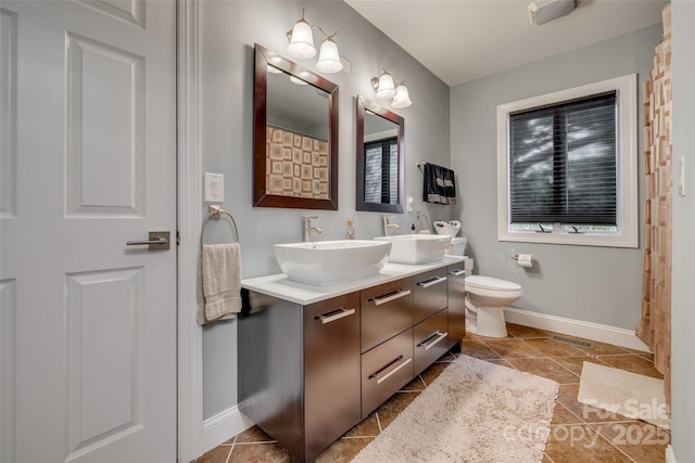 bathroom featuring toilet, double vanity, a sink, and baseboards