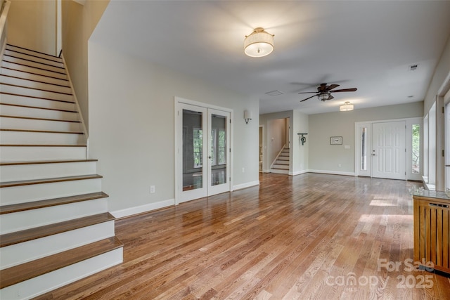 unfurnished living room featuring light wood-type flooring, baseboards, a ceiling fan, radiator heating unit, and stairs