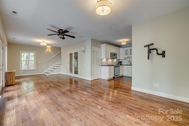 unfurnished living room with baseboards, a ceiling fan, light wood-type flooring, radiator, and stairs