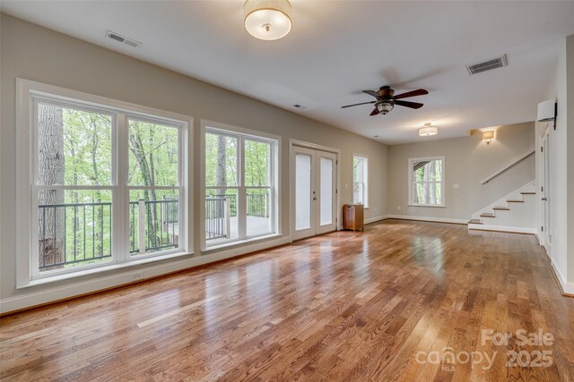 unfurnished living room featuring visible vents, baseboards, stairway, and a ceiling fan