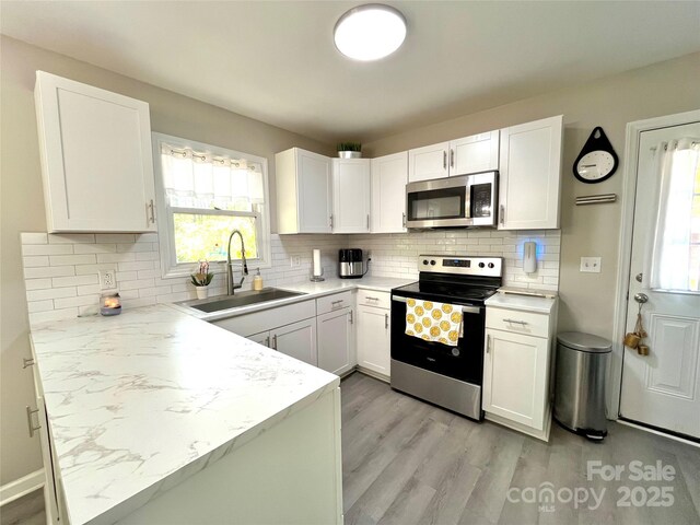 kitchen featuring light wood finished floors, white cabinets, a sink, backsplash, and appliances with stainless steel finishes