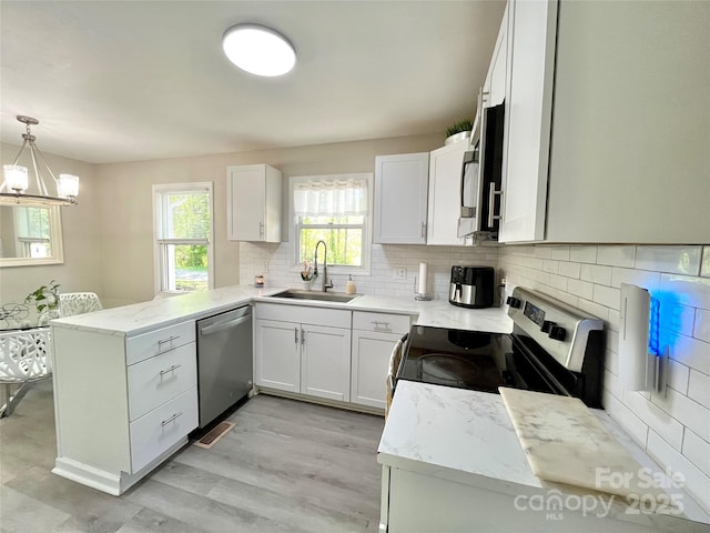 kitchen featuring a peninsula, a sink, backsplash, light stone counters, and appliances with stainless steel finishes