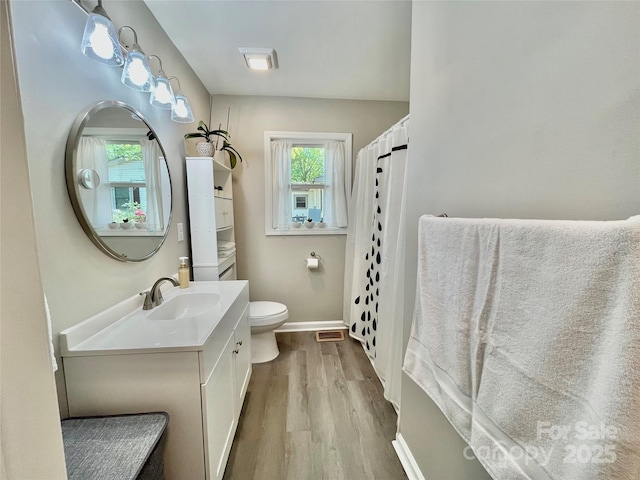 full bathroom with toilet, visible vents, baseboards, wood finished floors, and vanity