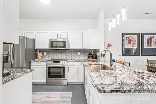 kitchen featuring appliances with stainless steel finishes, a sink, a peninsula, white cabinets, and light stone countertops