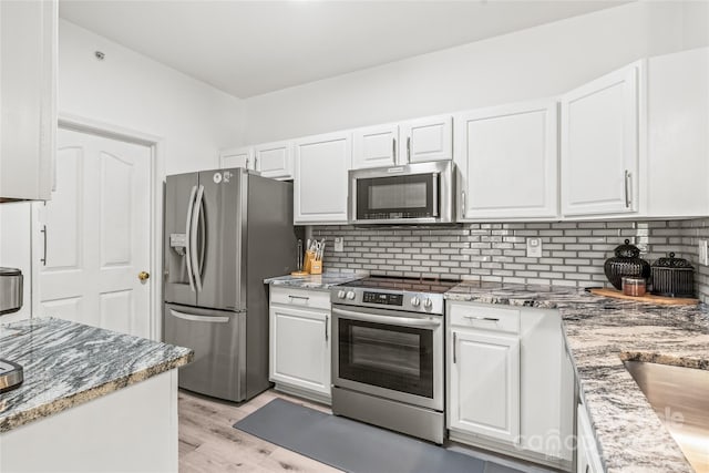 kitchen with appliances with stainless steel finishes, white cabinetry, decorative backsplash, and light wood finished floors
