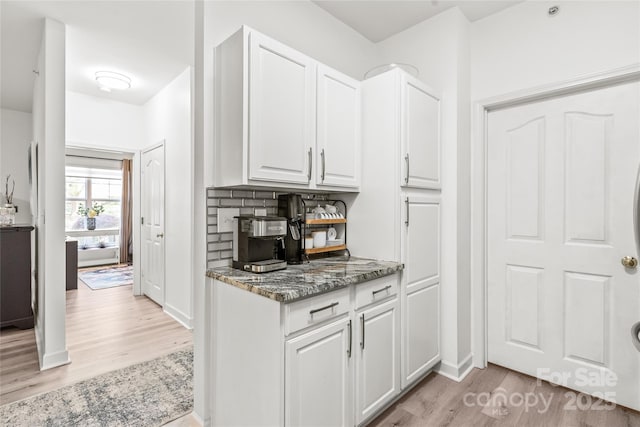 kitchen with light wood-style flooring, dark stone countertops, white cabinets, and baseboards