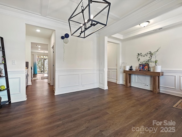 unfurnished dining area featuring dark wood-style flooring, a decorative wall, a chandelier, and crown molding