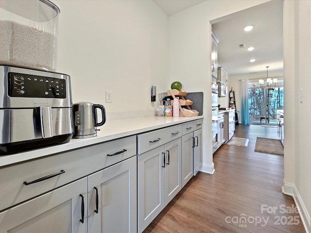kitchen with a notable chandelier, baseboards, recessed lighting, light countertops, and wood finished floors
