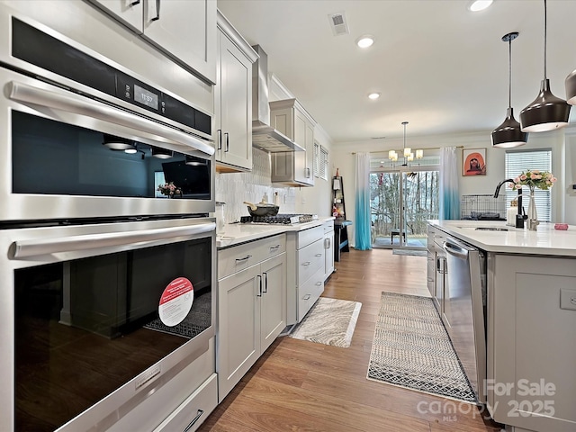 kitchen with tasteful backsplash, visible vents, wall chimney range hood, a chandelier, and stainless steel appliances