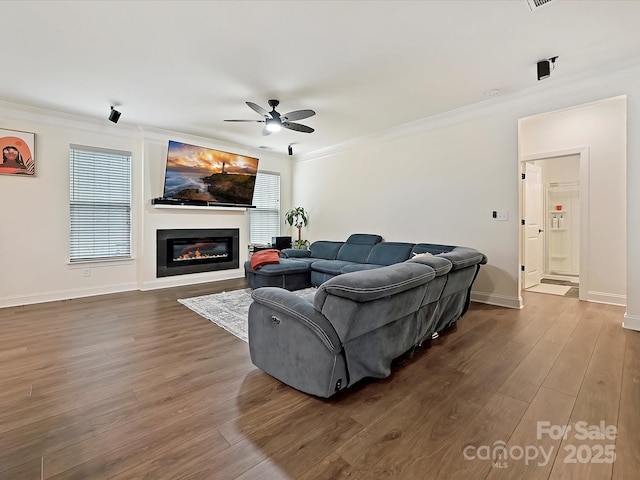 living area featuring dark wood-type flooring, crown molding, ceiling fan, and a glass covered fireplace