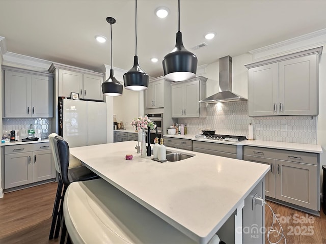 kitchen featuring gray cabinets, visible vents, stainless steel gas cooktop, wall chimney exhaust hood, and a sink
