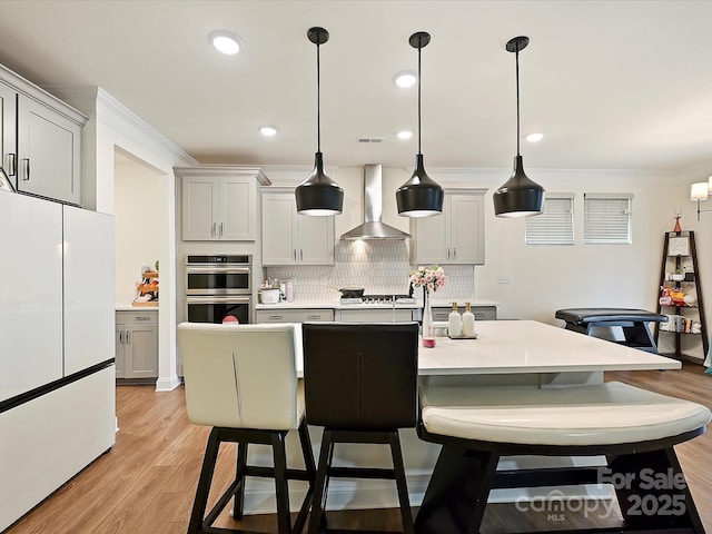 kitchen with wall chimney range hood, light countertops, freestanding refrigerator, crown molding, and stainless steel double oven