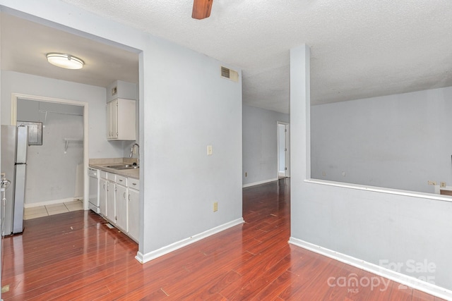 interior space featuring visible vents, a sink, freestanding refrigerator, white cabinetry, and wood finished floors