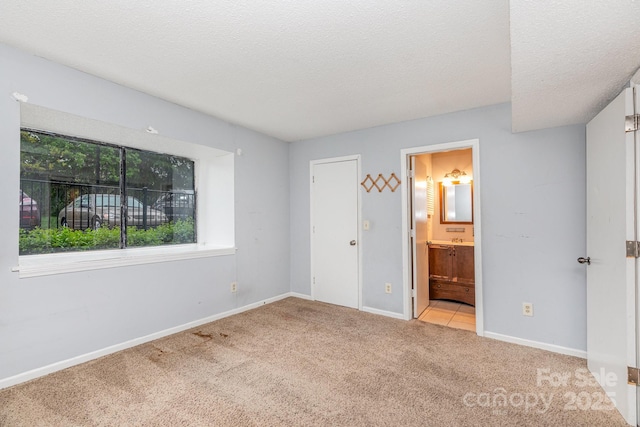 unfurnished bedroom featuring a textured ceiling, ensuite bathroom, baseboards, and carpet floors