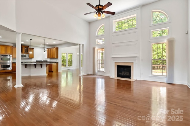 7302 Yellowhorn Trl, Waxhaw, NC 28173 - unfurnished living room featuring ornate columns, a towering ceiling, a ceiling fan, dark wood-style floors, and a fireplace with flush hearth