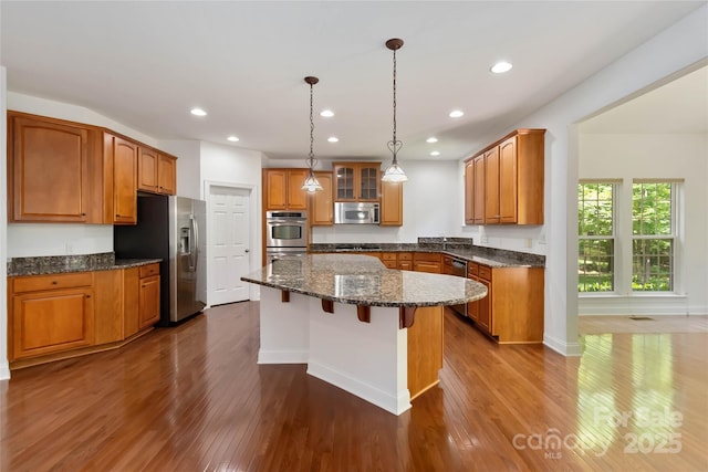 7302 Yellowhorn Trl, Waxhaw, NC 28173 - kitchen featuring appliances with stainless steel finishes, a center island, dark wood-type flooring, brown cabinets, and a kitchen bar