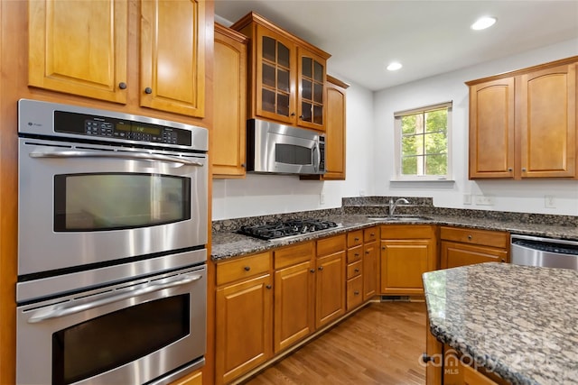 7302 Yellowhorn Trl, Waxhaw, NC 28173 - kitchen featuring appliances with stainless steel finishes, a sink, light wood-style floors, glass insert cabinets, and dark stone counters