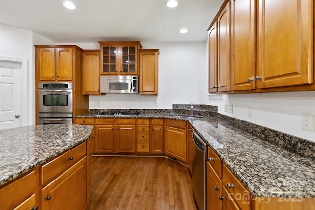 7302 Yellowhorn Trl, Waxhaw, NC 28173 - kitchen featuring appliances with stainless steel finishes, dark wood-style floors, a sink, brown cabinetry, and dark stone counters