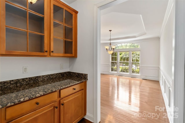 7302 Yellowhorn Trl, Waxhaw, NC 28173 - kitchen featuring a chandelier, wood finished floors, glass insert cabinets, dark stone countertops, and a decorative wall