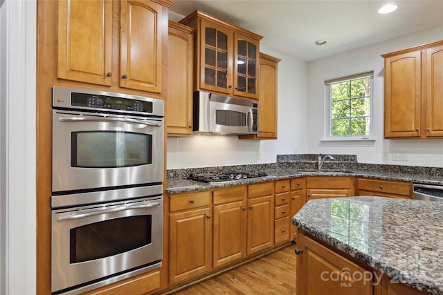 7302 Yellowhorn Trl, Waxhaw, NC 28173 - kitchen featuring appliances with stainless steel finishes, dark stone countertops, light wood-type flooring, glass insert cabinets, and brown cabinets