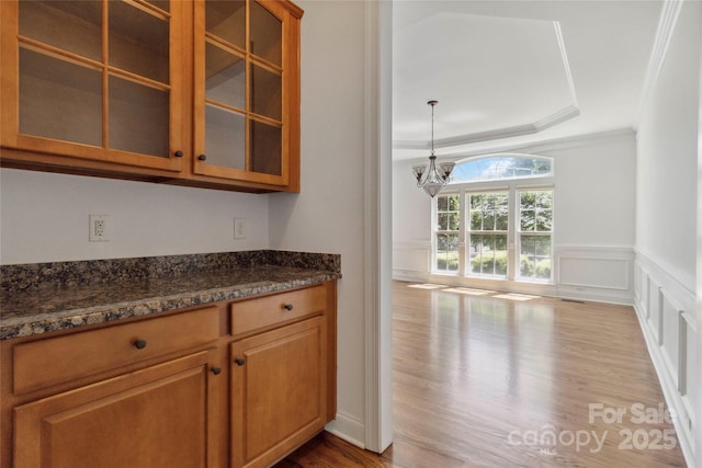 7302 Yellowhorn Trl, Waxhaw, NC 28173 - kitchen with wood finished floors, glass insert cabinets, a chandelier, brown cabinets, and ornamental molding