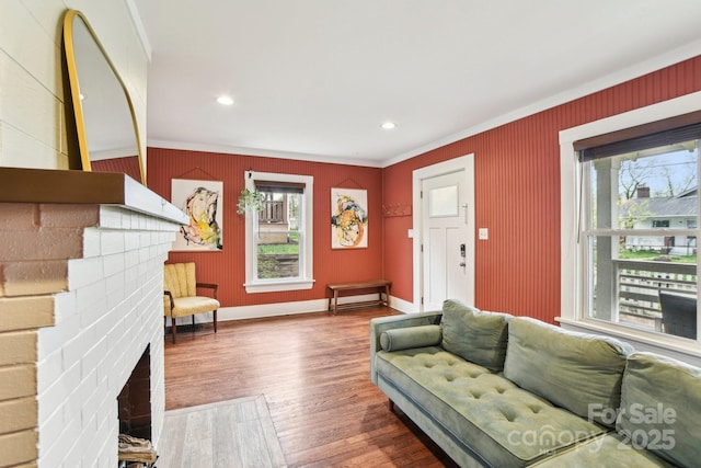living area featuring baseboards, recessed lighting, crown molding, a brick fireplace, and wood finished floors
