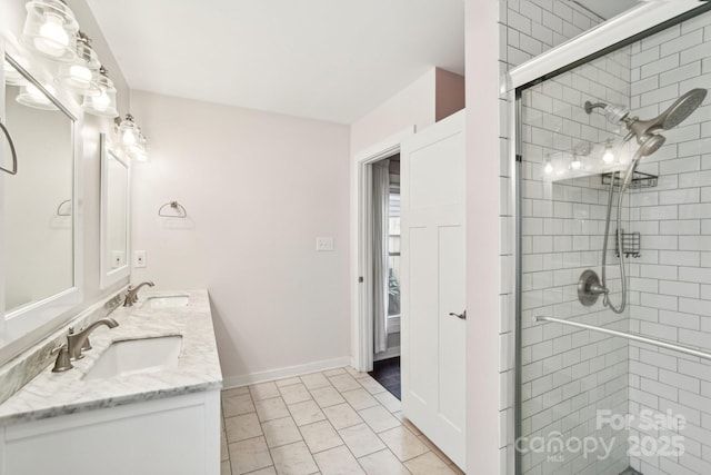 full bath with a sink, baseboards, a shower stall, and double vanity