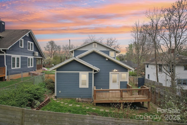 back of house at dusk with a fenced backyard and a wooden deck