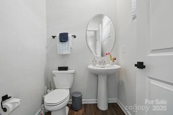 half bathroom featuring baseboards, wood finished floors, and toilet