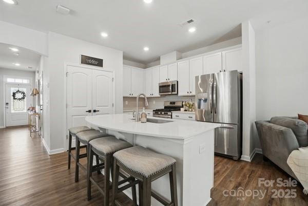kitchen featuring stainless steel appliances, baseboards, dark wood-style floors, and a kitchen bar