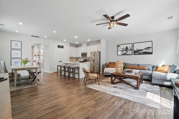 living area featuring wood finished floors, ceiling fan, arched walkways, visible vents, and recessed lighting