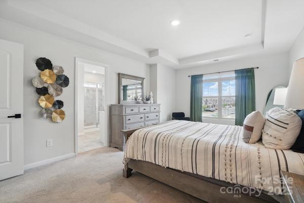 carpeted bedroom featuring a tray ceiling, baseboards, ensuite bathroom, and recessed lighting