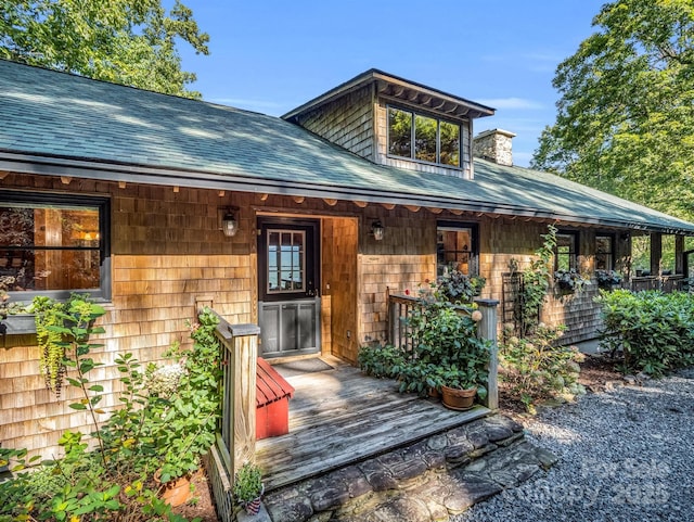 entrance to property with roof with shingles, a chimney, and covered porch