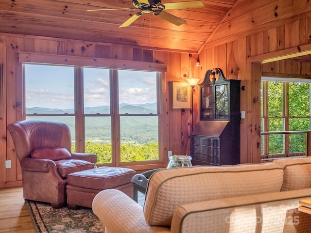 living area featuring wooden walls, a ceiling fan, wood ceiling, lofted ceiling, and a mountain view