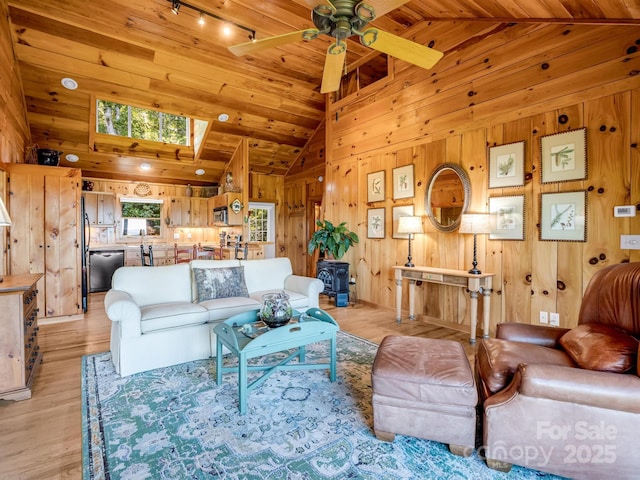 living area featuring track lighting, light wood-style flooring, a ceiling fan, wood walls, and a skylight