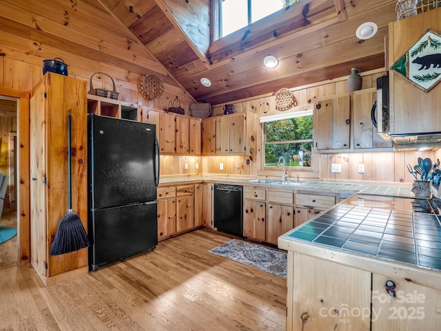kitchen featuring a sink, wooden walls, black appliances, vaulted ceiling, and tile countertops