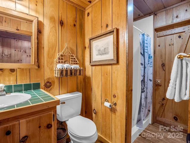 full bathroom featuring wood walls, curtained shower, vanity, and toilet