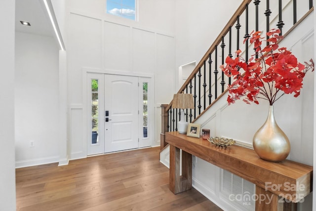 entrance foyer featuring stairs, hardwood / wood-style flooring, a towering ceiling, and a decorative wall