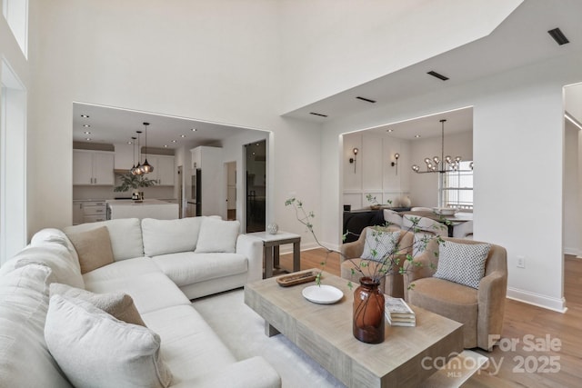 living room featuring a chandelier, light wood-style floors, baseboards, and a towering ceiling