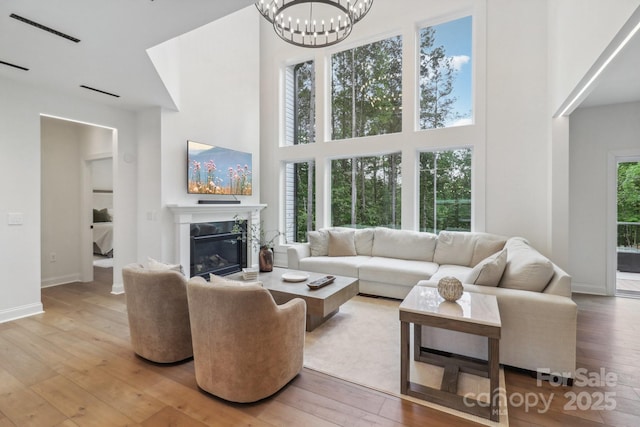 living room with a high ceiling, light wood finished floors, a chandelier, a high end fireplace, and baseboards