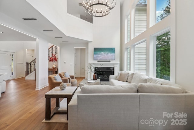 living room with stairs, light wood-style floors, a chandelier, a premium fireplace, and a towering ceiling