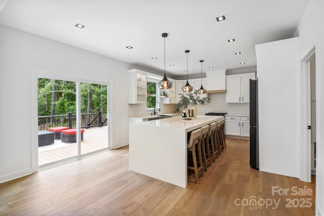 kitchen with a sink, a center island, freestanding refrigerator, backsplash, and white cabinetry