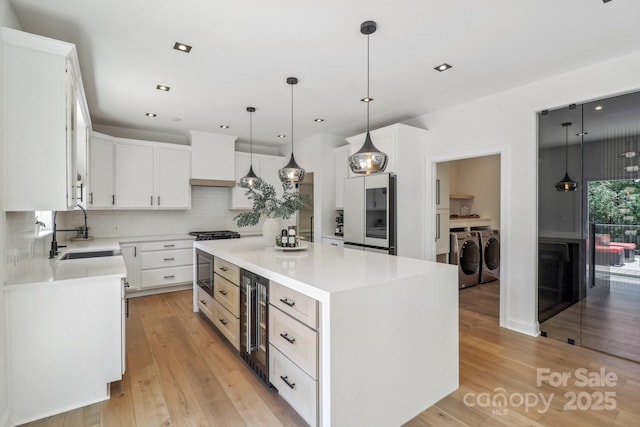 kitchen with a sink, backsplash, wine cooler, washing machine and clothes dryer, and a center island