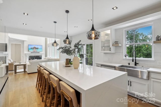kitchen featuring a sink, white cabinetry, backsplash, light wood-style flooring, and light countertops