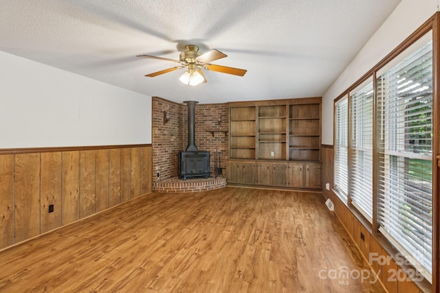 119 Legacy Ln, Harmony, NC 28634 - unfurnished living room featuring a wood stove, light wood-style floors, wainscoting, ceiling fan, and wood walls