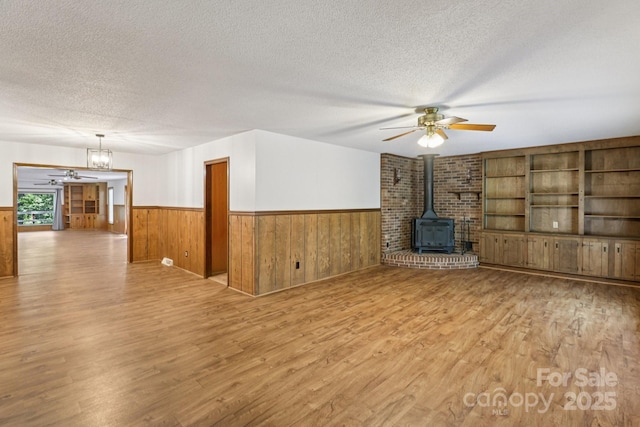 119 Legacy Ln, Harmony, NC 28634 - unfurnished living room with ceiling fan, a textured ceiling, a wainscoted wall, wood finished floors, and a wood stove