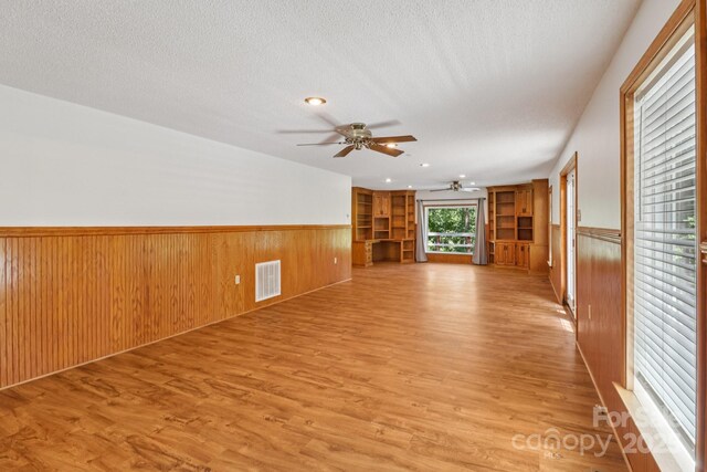 119 Legacy Ln, Harmony, NC 28634 - unfurnished living room with a ceiling fan, a wainscoted wall, wood walls, light wood-style flooring, and a textured ceiling