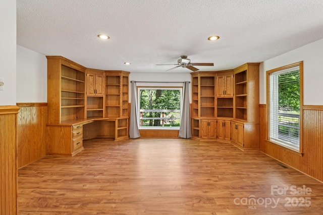 119 Legacy Ln, Harmony, NC 28634 - unfurnished living room with light wood-style flooring, built in desk, wainscoting, ceiling fan, and a textured ceiling